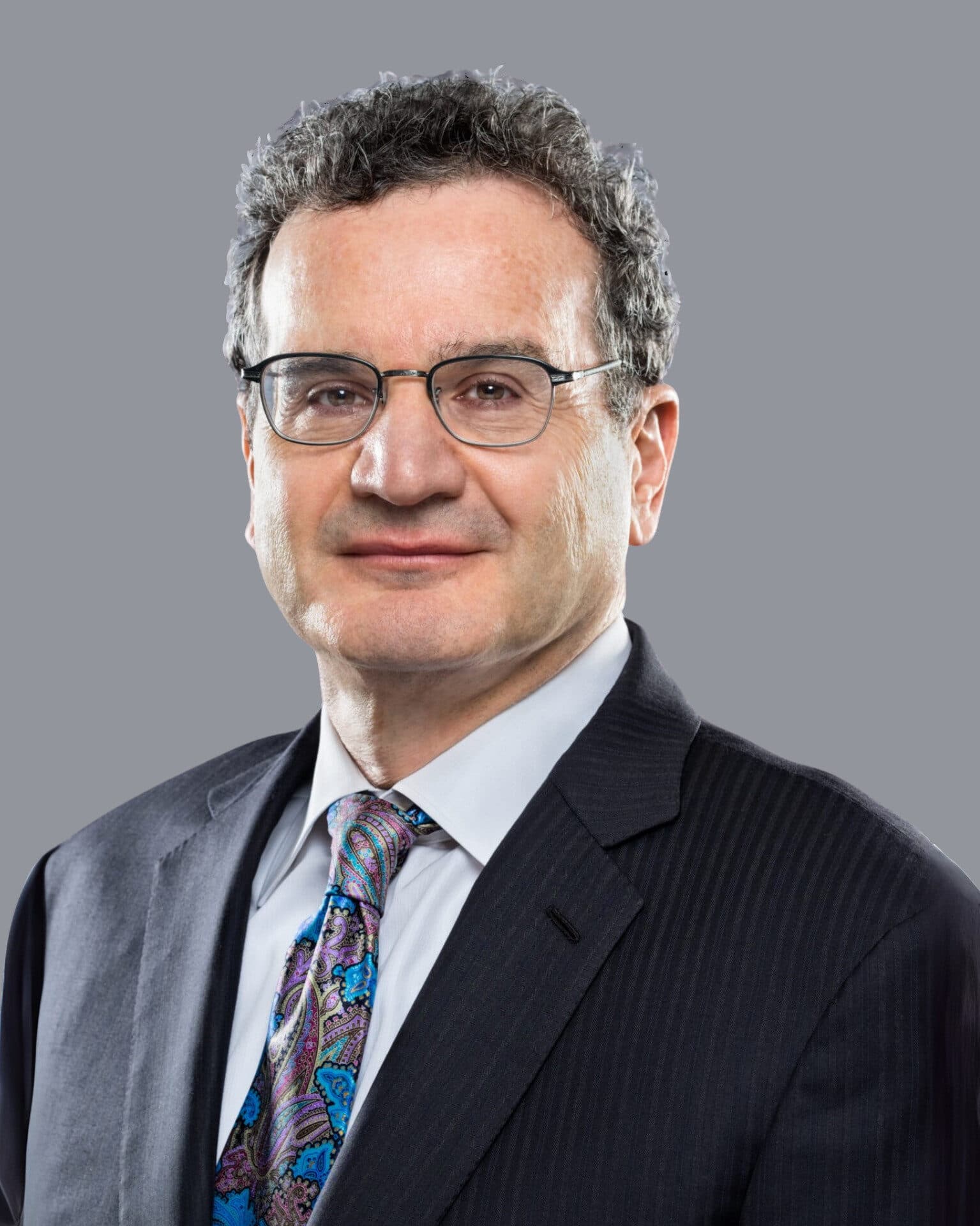 Middle-aged man with glasses and grey hair wearing a pinstripe suit and colorful paisley tie.